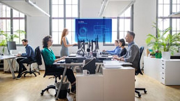 Employees sitting at a table watching a presentation with the OpenBlue Enterprise Manager overlaid on the screen